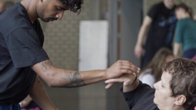 Two dancers with their eyes closed touch one hand in the middle, sensing each other's presence
