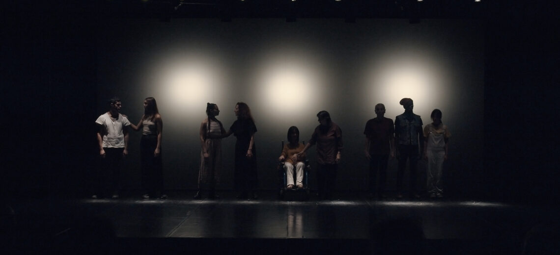 nine performers are on a dark stage, slightly lit from behind. They are divided into three couples and a trio