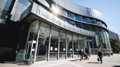 The TNB venue is a large building designed in a contemporary architectural style. Its entrance features glass walls, while the rest of the structure is gray.