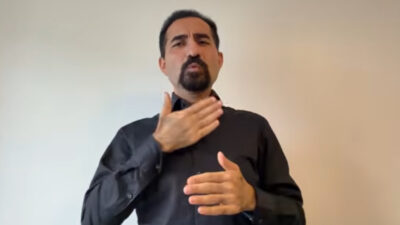 A Deaf man signing. He wears a black shirt. The background is white.