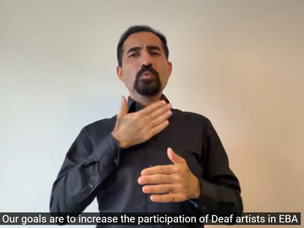 A Deaf man signing. He wears a black shirt. The background is white.